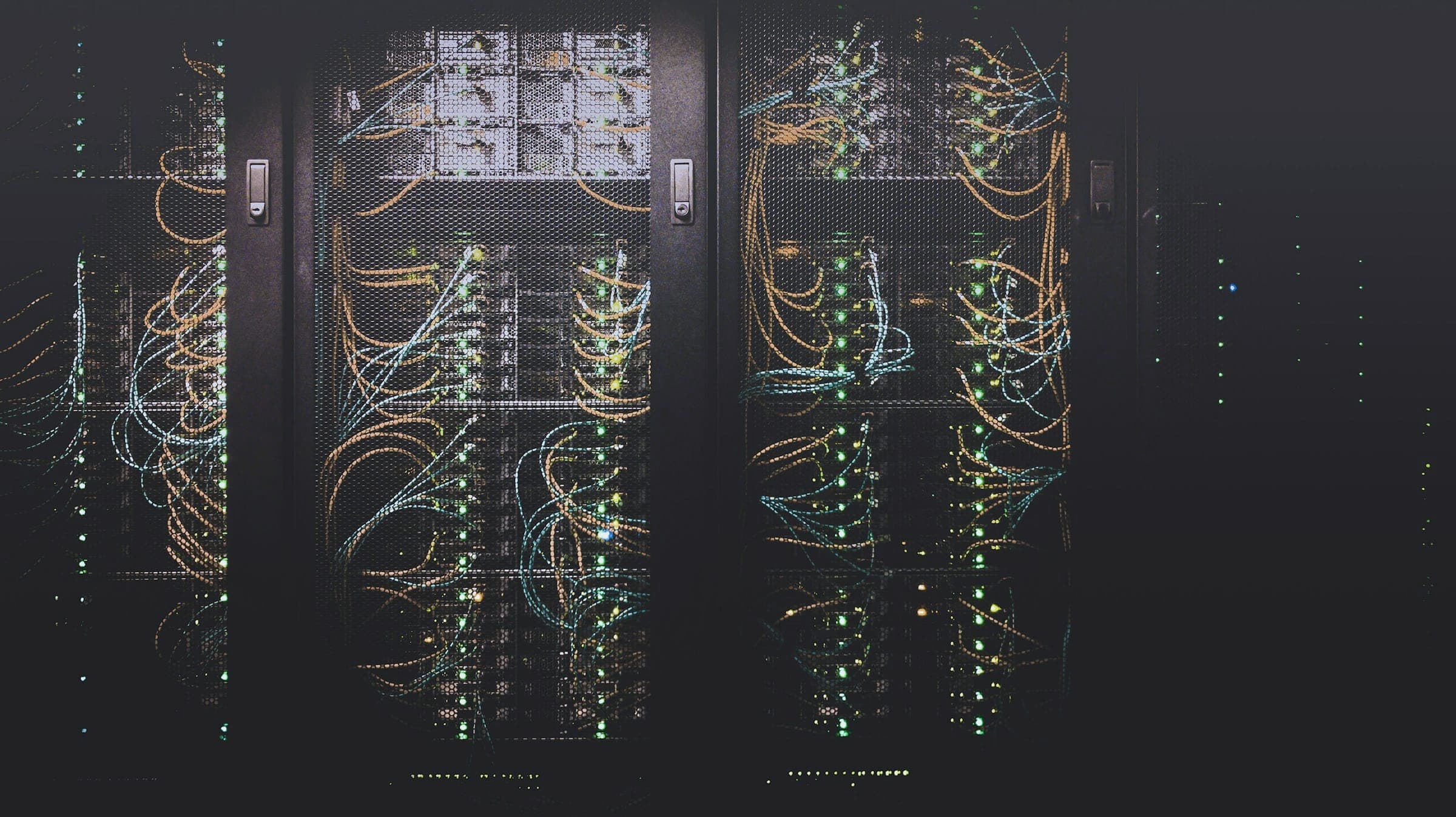 Two open server cabinets in a dark room, dense patch cabling and small green status lights.