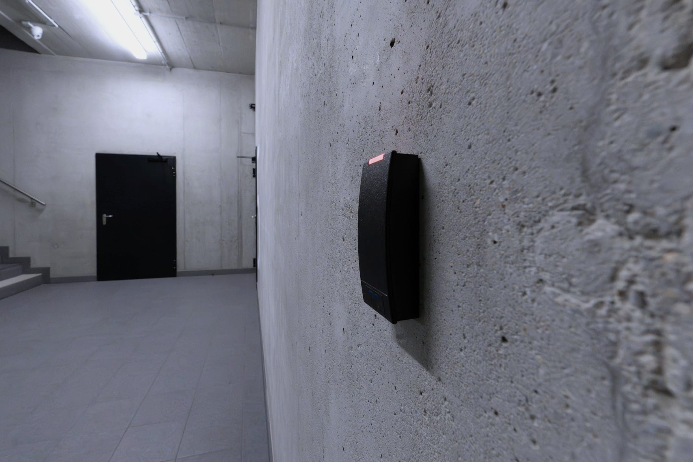 A wall-mounted access card reader beside a corridor leading to a dark door.