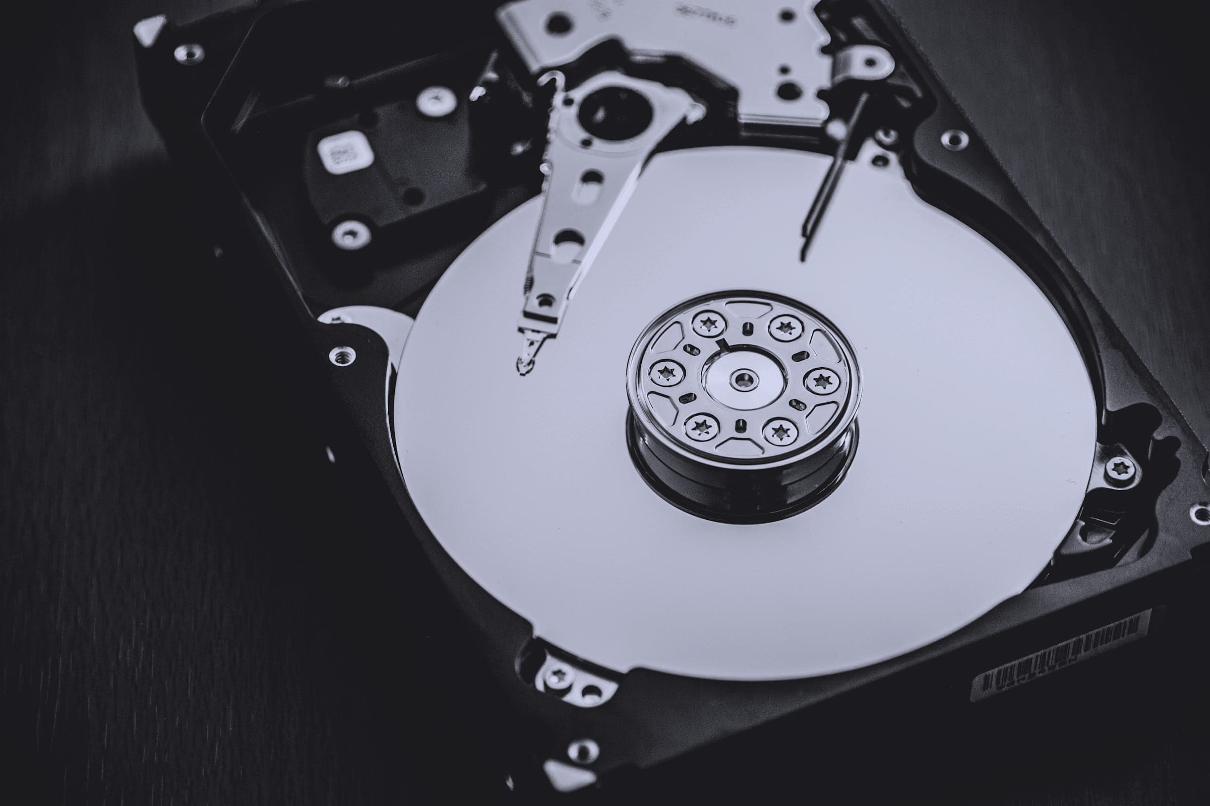 An opened hard disk drive showing the platter and read arm, in dark monochrome.