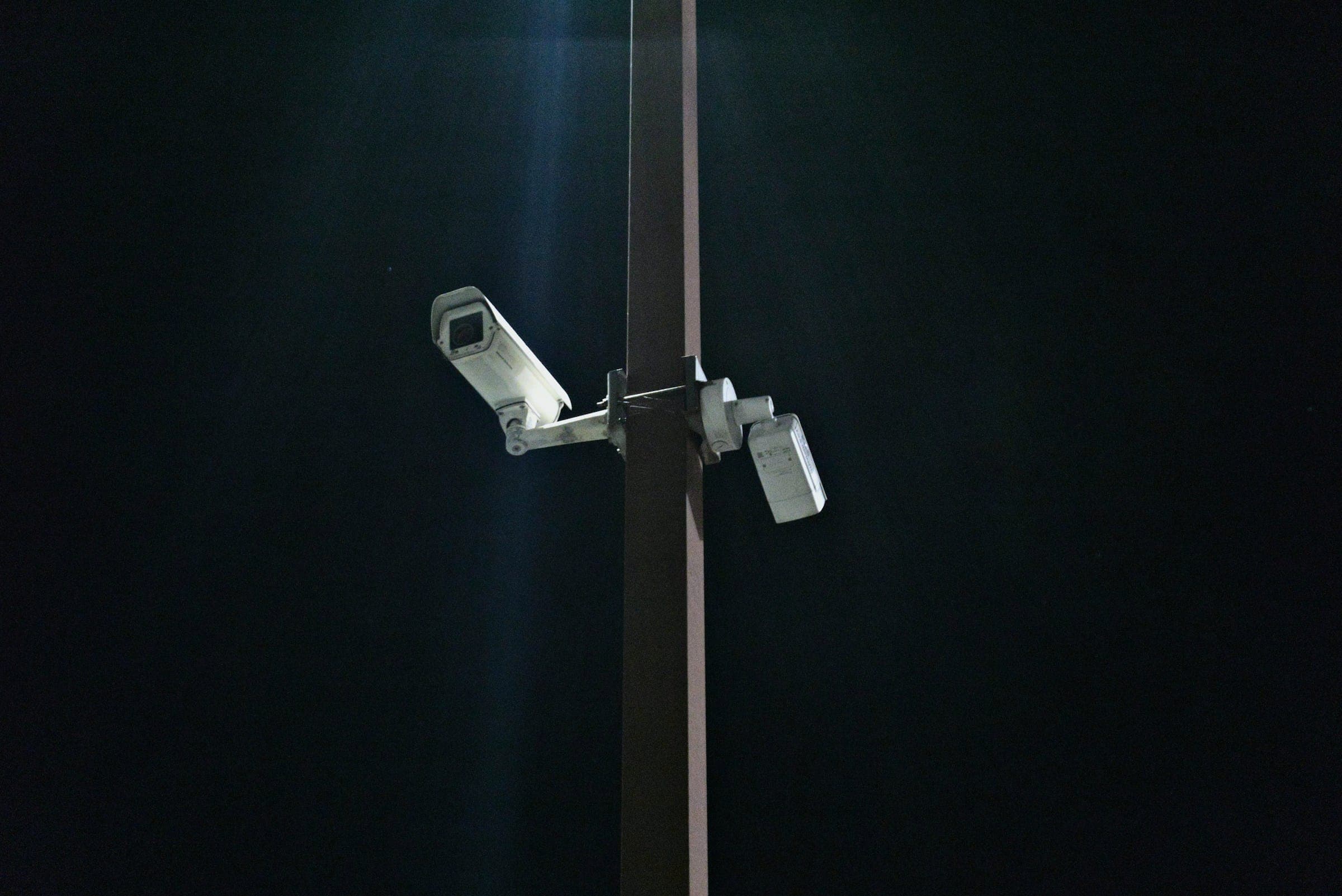 Two security cameras on a tall pole against a dark night sky.
