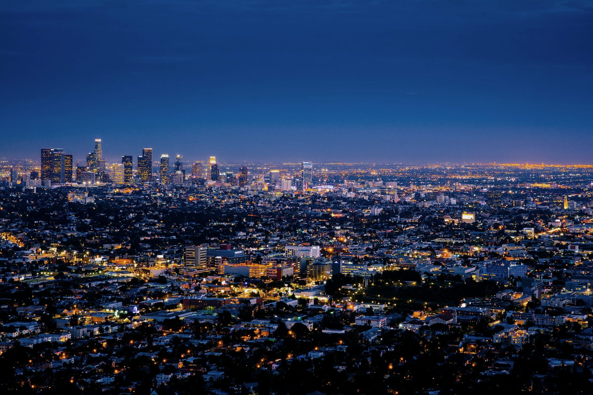 A wide city skyline at dusk under a deep blue sky with a sea of lights below.