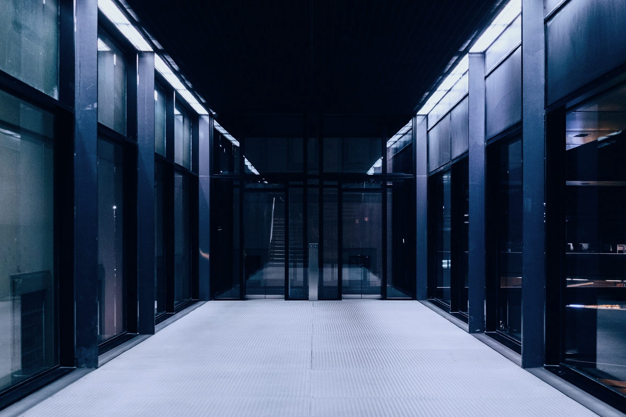 A long, dark aisle between tall glass-fronted cabinets lit by cool overhead strips.